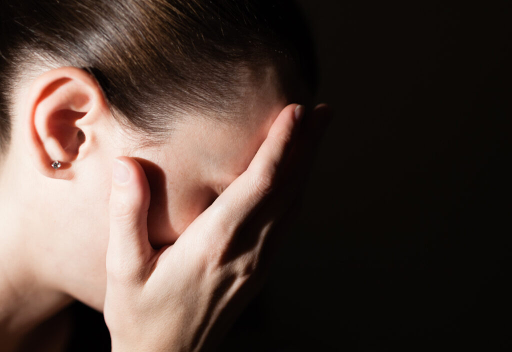 Woman with her hands clasp over face feeling sad.