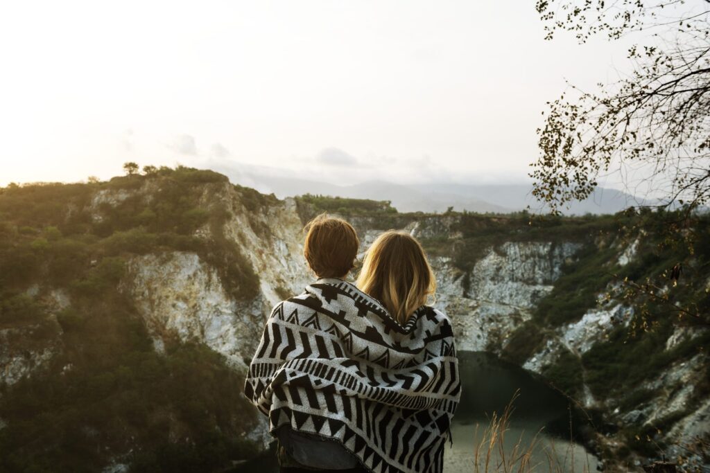 Couple Wrapped in a Blanket staring out at a lake and mountains cropped